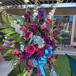 Tall floral standing spray with purple, pink, and blue flowers and a blue ribbon
