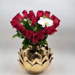 Red roses arranged in a gold lotus-shaped vase with one white orchid bloom