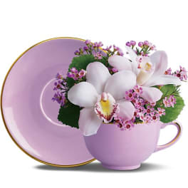 Pink teacup and saucer holding white orchids and purple filler flowers