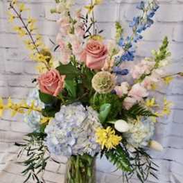 Mixed pastel bouquet in a glass vase with pink roses and blue hydrangeas