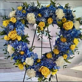 Heart-shaped floral wreath with blue, yellow, and white flowers on an easel