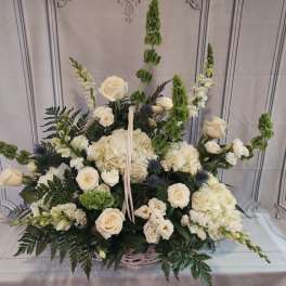 White floral basket arrangement with roses, hydrangeas, and tall green spikes
