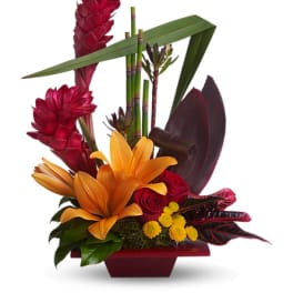 Tropical flower arrangement with orange lilies, red blooms, and bamboo accents in a red vase