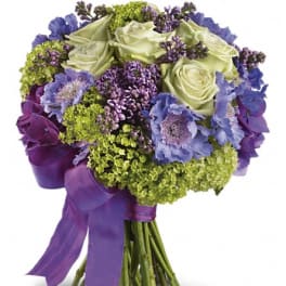 Bouquet of pale green roses, purple flowers, and blue blooms tied with a purple ribbon
