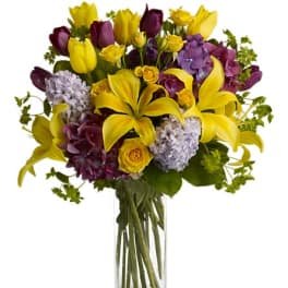 Yellow lilies and purple flowers arranged in a clear glass vase