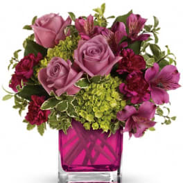 Pink roses and purple flowers arranged in a magenta glass vase