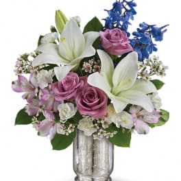 Bouquet of white lilies, pink roses, and blue flowers in a silver vase