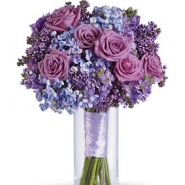 Purple roses and blue-purple flowers in a clear glass vase