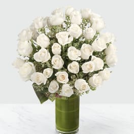 White roses arranged in a tall green glass vase