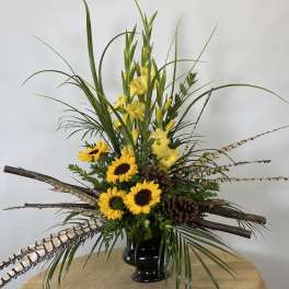 Tall arrangement of yellow flowers and sunflowers in a black vase