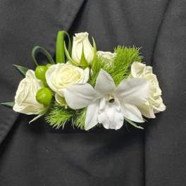 White rose and orchid boutonniere with green accents on a dark suit