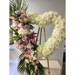 Heart-shaped floral wreath with white hydrangeas, pink roses, and lilies on an easel