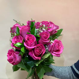 Handheld bouquet of bright pink roses with small white filler flowers