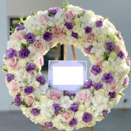 Large floral wreath of pink, purple, and white blooms on an easel with a blank sign
