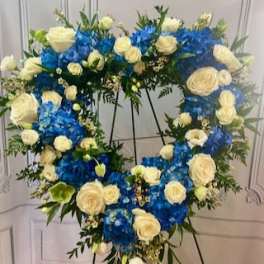 Heart-shaped floral wreath with blue and white roses on a stand