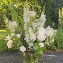 Tall white floral arrangement in a clear glass vase outdoors