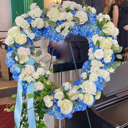 Heart-shaped floral wreath of white roses and blue hydrangeas on an easel
