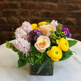 Mixed bouquet in a square glass vase with peach roses and yellow ranunculus