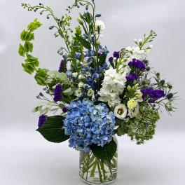 Blue hydrangeas and white flowers in a clear glass vase