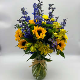 Bouquet of sunflowers, blue delphinium, and yellow alstroemeria in a glass vase