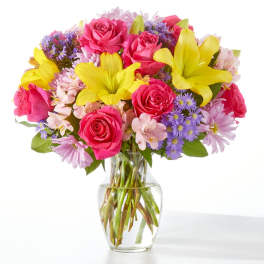 Bouquet of pink roses, yellow lilies, and purple daisies in a glass vase