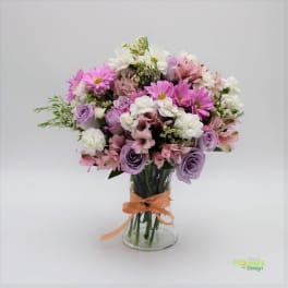 Bouquet of pink, white, and lavender flowers in a glass vase with an orange ribbon
