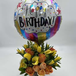 Birthday balloon above a bouquet of yellow calla lilies and peach roses in a vase