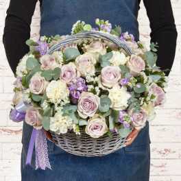 Basket of pale roses, white carnations, and purple flowers with ribbon