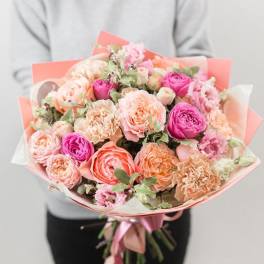 Handheld bouquet of pink and peach roses wrapped in coral paper