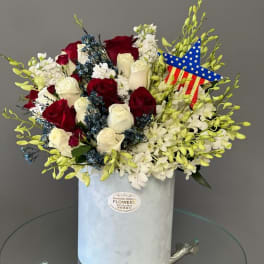 Red and white roses in a white hat box with a patriotic star decoration.