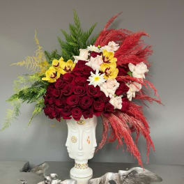 Large floral arrangement in a white sculptural vase with red, yellow, and white blooms