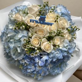 Blue hydrangea bouquet with white roses and a baby boy topper