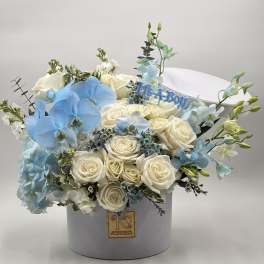 White roses and blue orchids arranged in a round hat box with a "It's a Boy" topper.