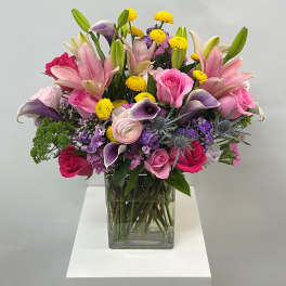 Mixed bouquet of pink lilies, roses, and purple flowers in a glass vase