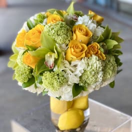 Yellow roses and white flowers arranged in a clear glass vase