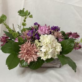 Mixed pink, white, and purple flowers arranged in a low wooden container