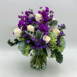 Purple and white flowers arranged in a clear glass vase