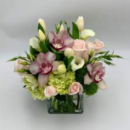 Pink orchids, roses, calla lilies, and tulips in a glass vase
