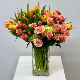 Pink roses and yellow tulips arranged in a clear glass vase.
