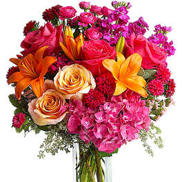 Bouquet of pink roses, orange lilies, and hot pink hydrangeas in a clear vase