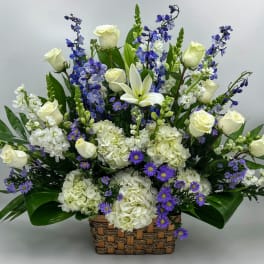 Large basket arrangement with white roses, hydrangeas, lilies, and purple flowers