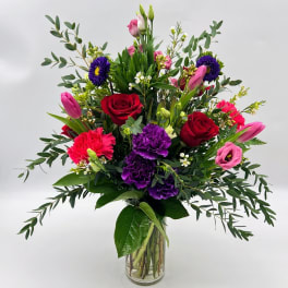 Mixed bouquet of roses, tulips, carnations, and purple blooms in a glass vase