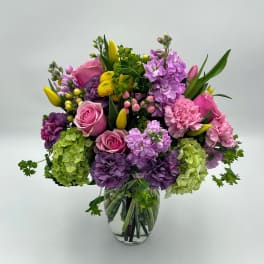 Mixed bouquet of pink, purple, and yellow flowers in a clear glass vase