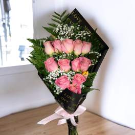 Bouquet of pink roses with baby's breath wrapped in black paper and tied with a pink ribbon