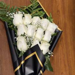Wrapped bouquet of white roses with baby's breath in black paper with gold trim and white ribbon.