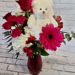 Red flowers arranged with a white teddy bear in a vase