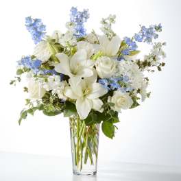 White lilies and roses in a clear glass vase with blue flowers