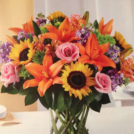 Mixed bouquet of sunflowers, orange lilies, and pink roses in a glass vase