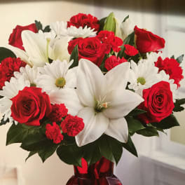 Red roses, white lilies, and white daisies in a red glass vase