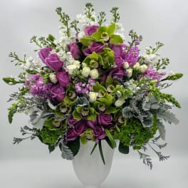 Purple roses and green orchids in a white vase